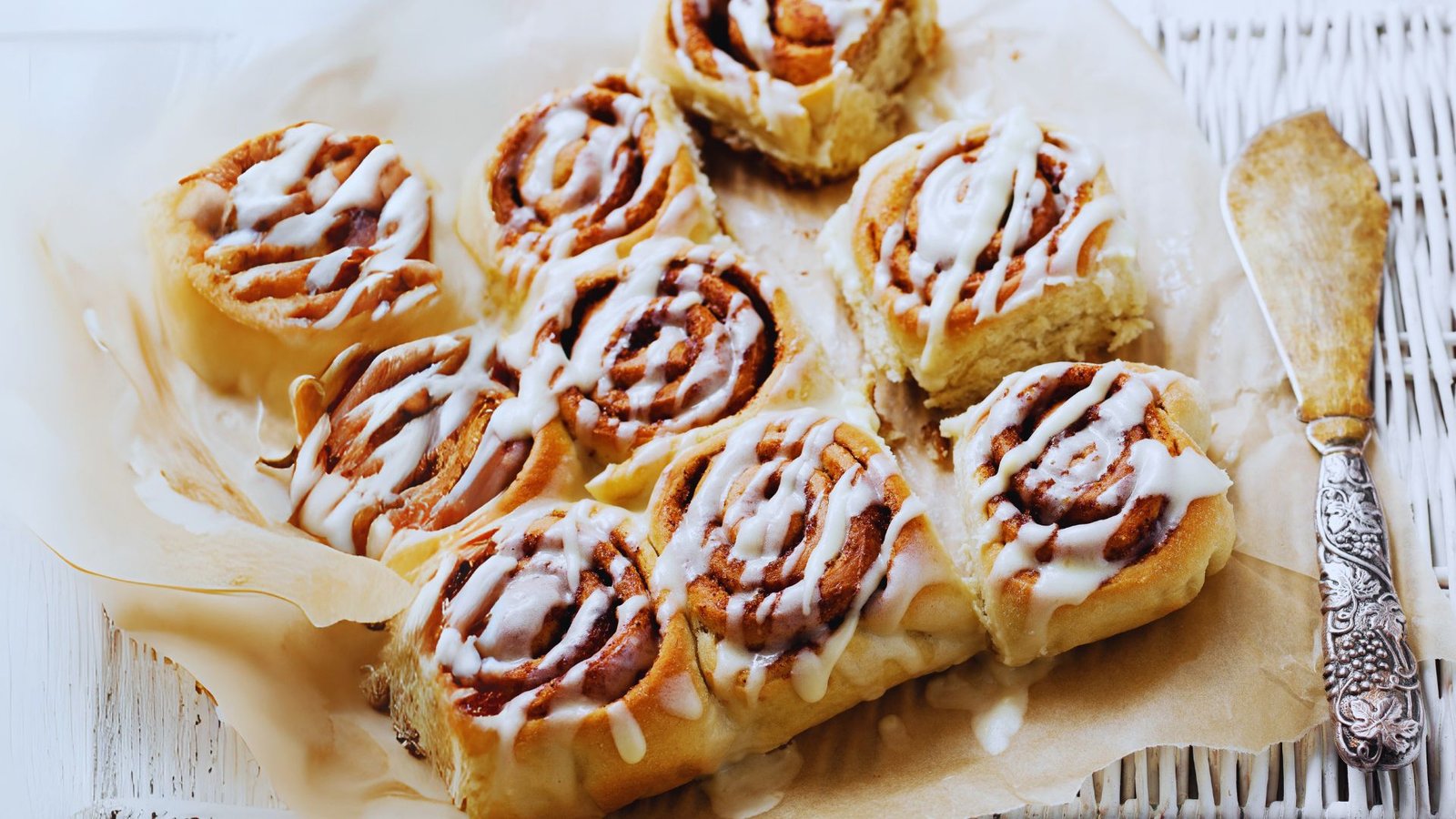 A close-up of freshly baked cinnamon rolls drizzled with icing, surrounded by star anise and cinnamon sticks.